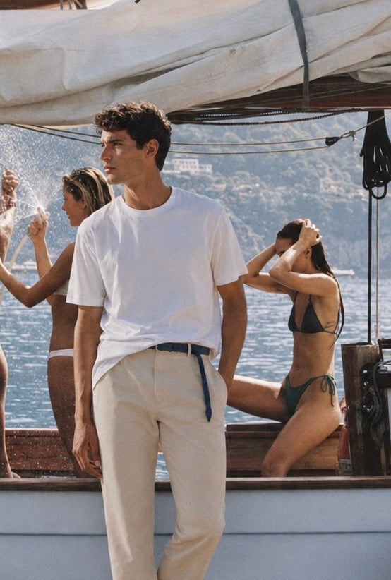 Modelo veste camiseta branca iA T-Shirt Sardegna Wellness a bordo no litoral mediterrâneo — camiseta masculina premium em Modal TENCEL